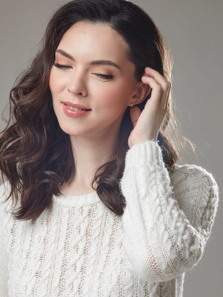 young caucasian model with long dark hair poses for the camera with hand near her face